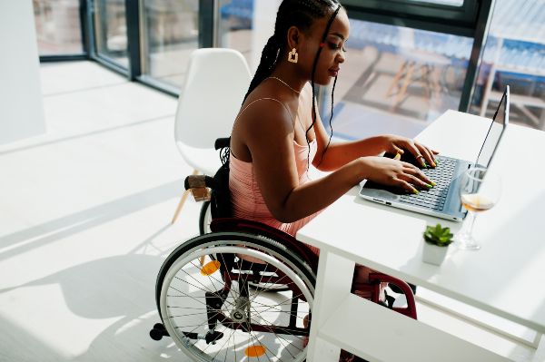 Características de LMS, joven mujer afroamericana en silla de ruedas en casa usando una plataforma LMS desde una laptop.