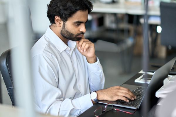 E learning ventajas y desventajas, Joven empleado indio ocupado trabajando en un portátil, mirando el ordenador en la oficina.
