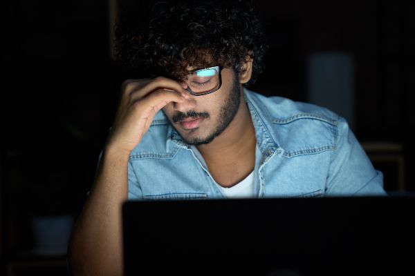 E learning ventajas y desventajas, Joven soñoliento con gafas usando la computadora trabajando hasta tarde.