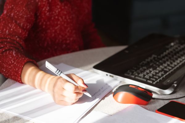 Características de la gamificación; presentación de la mano de una joven tomando notas mientras está cerca de su computadora portátil.