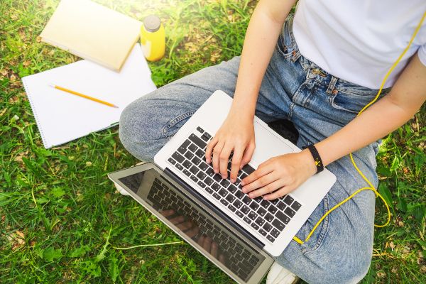 Características de la gamificación; imagen de un joven sentado en un área verde con su computadora portátil y otros accesorios escolares de manera agradable.