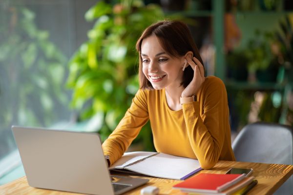 Gamificación ventajas y desventajas; imagen de una mujer feliz frente a su computadora portátil revisando una serie de cursos online para implementar de manera efectiva la gamificación.