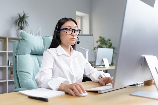 LMS ventajas; imagen de una mujer con auriculares frente a su computadora tomando diversas estrategias online para su aprendizaje empresarial.