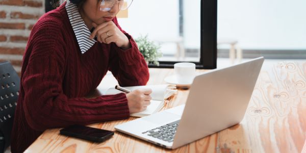 Capacitación corporativa; imagen de una joven prestando mucha tención y haciendo notas mientras recibe una capacitación de manera digital.