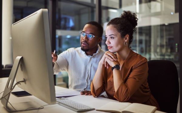 Capacitación corporativa; imagen de una mujer recibiendo una capacitación por su compañero haciendo uso de plataformas digitales.