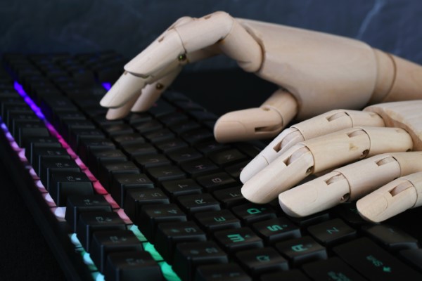 Inteligencia artificial en la educación; imagen de un robot escribiendo con el teclado de una computadora siendo el trabajo en conjunto que realiza la IA para una educación de calidad e innovadora.