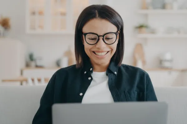 Mujer sonriendo, mientras toma clases en línea.